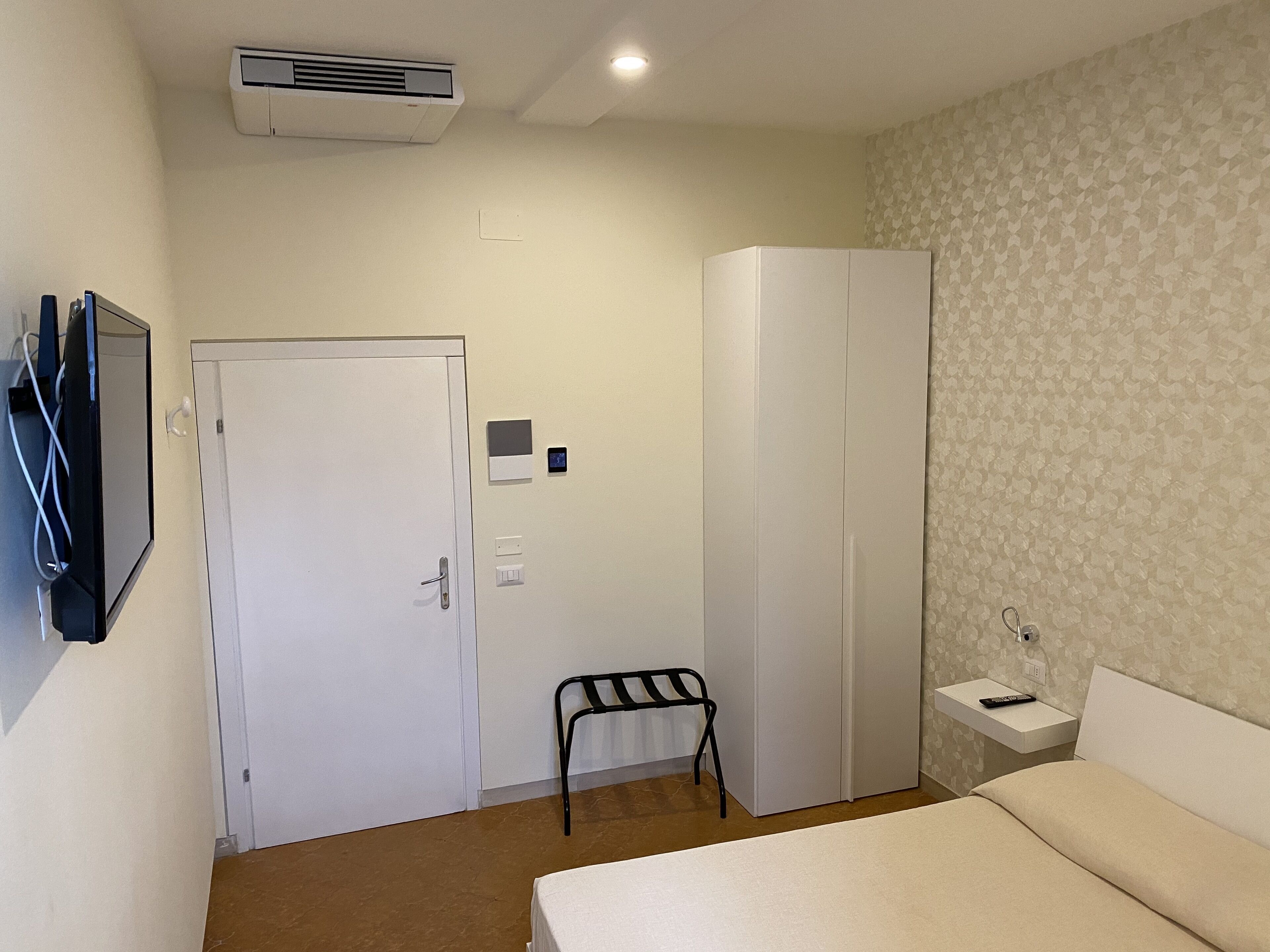 Une chambre d’hôtel comprenant un lit, une armoire, une petite table avec une télécommande, une chaise et un climatiseur fixé au mur.