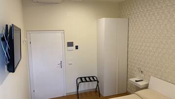 Une chambre d’hôtel comprenant un lit, une armoire, une petite table avec une télécommande, une chaise et un climatiseur fixé au mur.