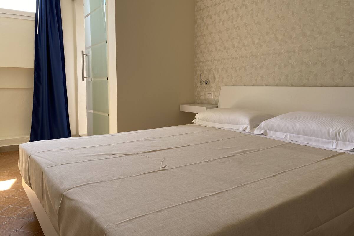 Ein Schlafzimmer mit einem Bett, einem Nachttisch, einer Wandleuchte und einer Wandtapete mit Muster.