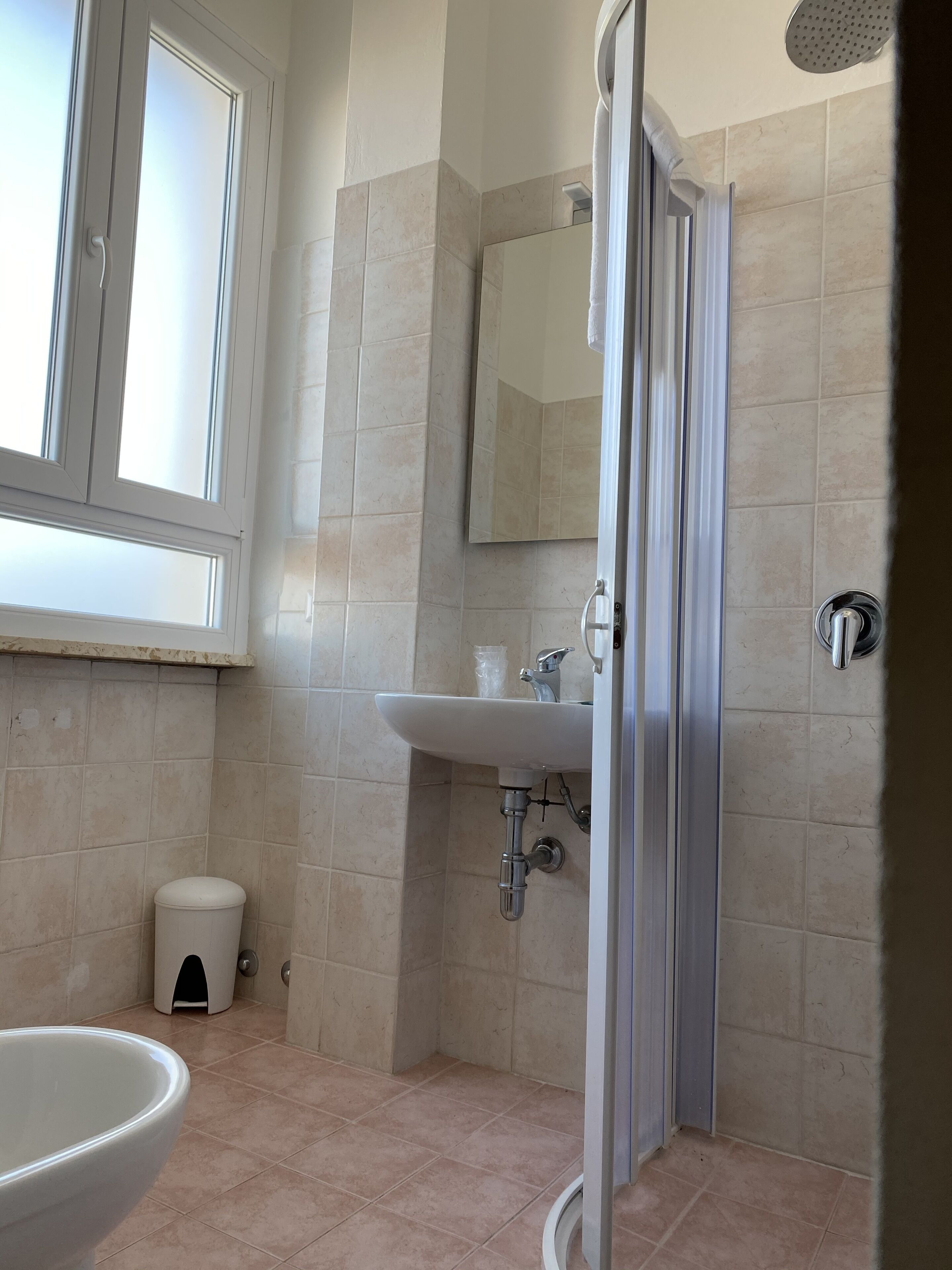 A bathroom with a shower, sink, toilet, and a window.