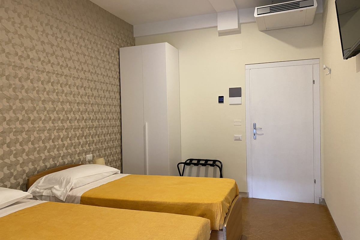 Ein Hotelzimmer mit zwei Betten, einem Kleiderschrank, einer Tür und einer Klimaanlage.