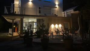 Un bâtiment à deux étages doté d’un balcon, d’un espace extérieur aménagé pour s’asseoir et de plantes en pot.