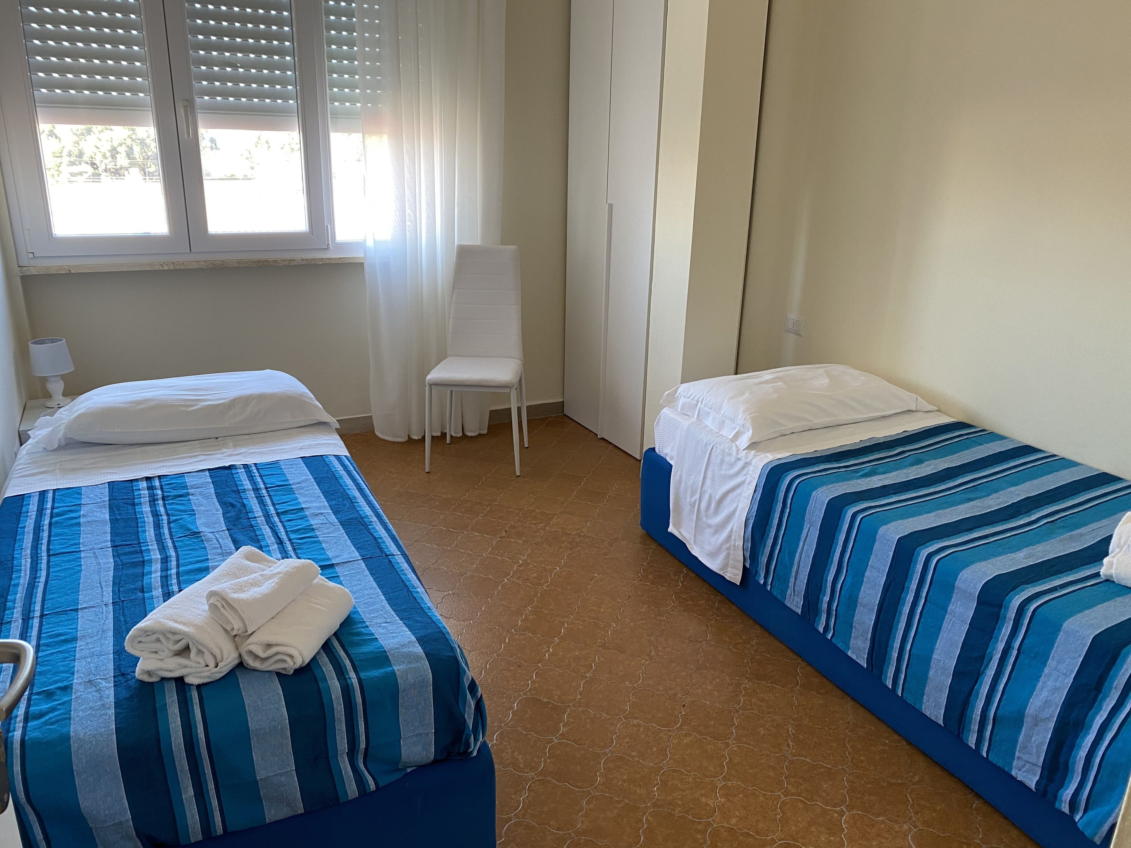 A hotel room with two beds, a chair, and a window with blinds.