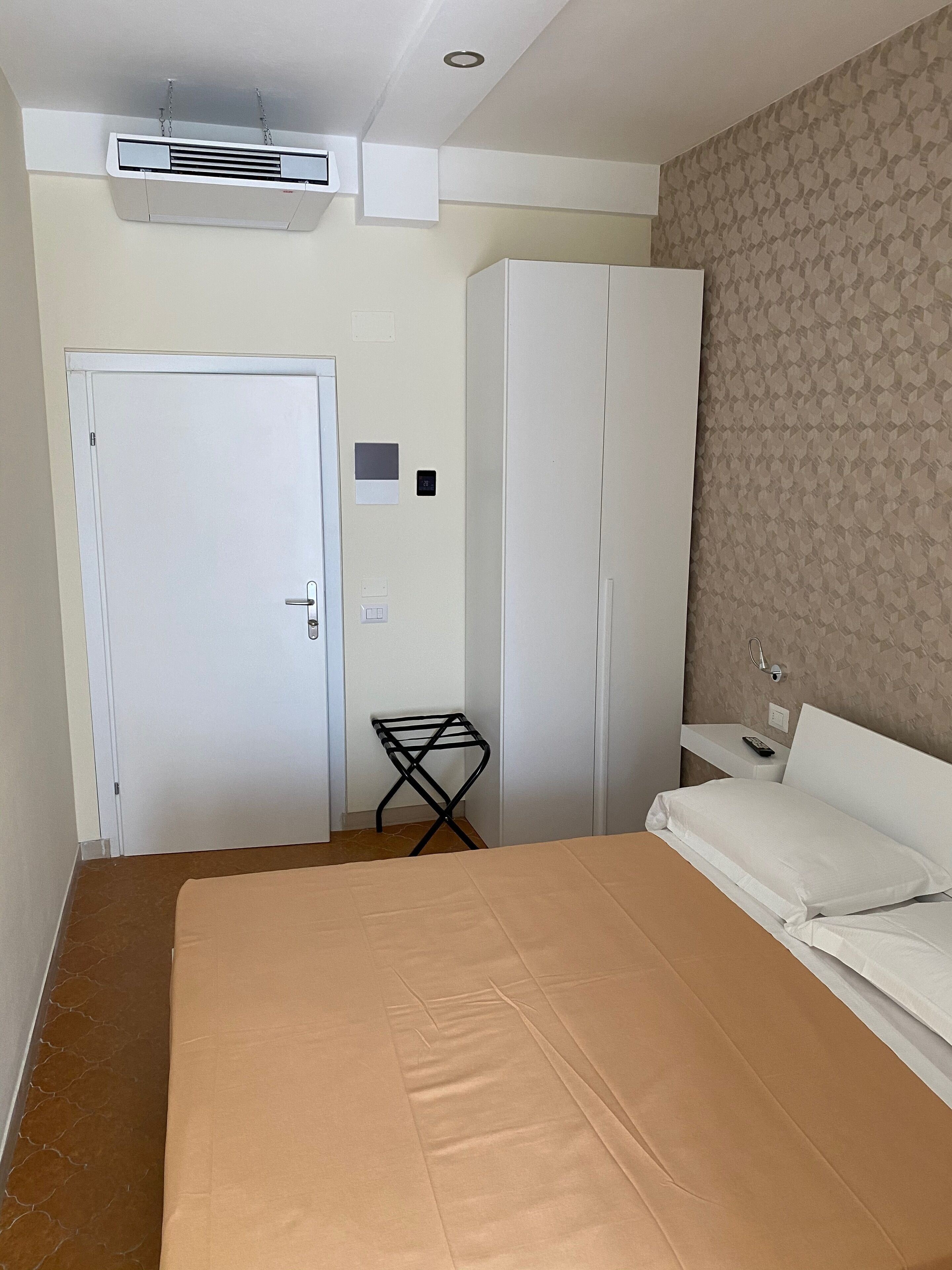A hotel room with a bed, wardrobe, and a small table with a chair.