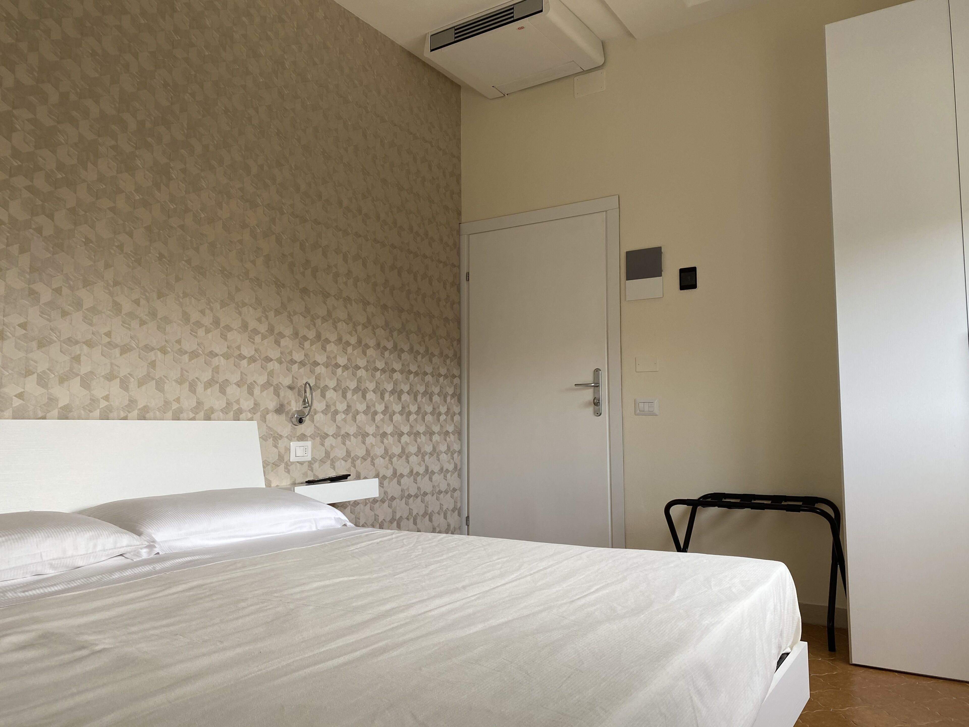 Een hotelkamer met een bed, een stoel, een deur en een wandgemonteerde airconditioner.