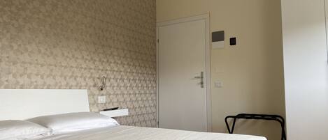 A hotel room with a bed, a chair, a door, and a wall-mounted air conditioner.