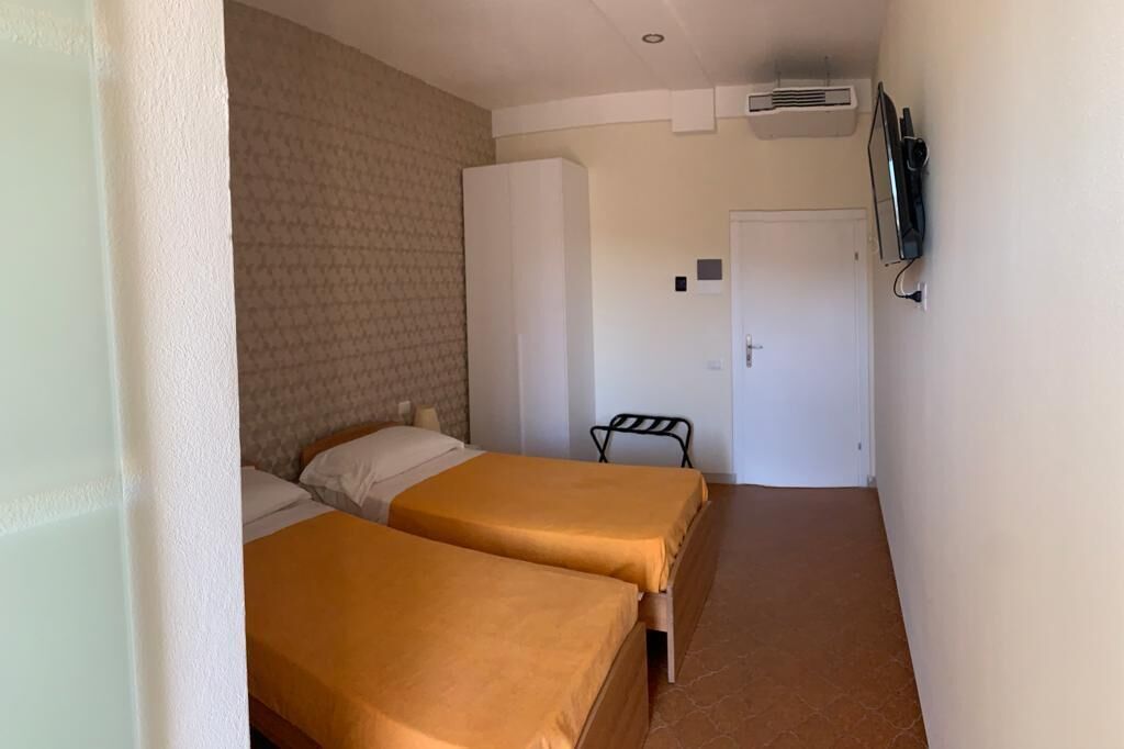 Una habitación de hotel pequeña con dos camas, un armario, un televisor y aire acondicionado.