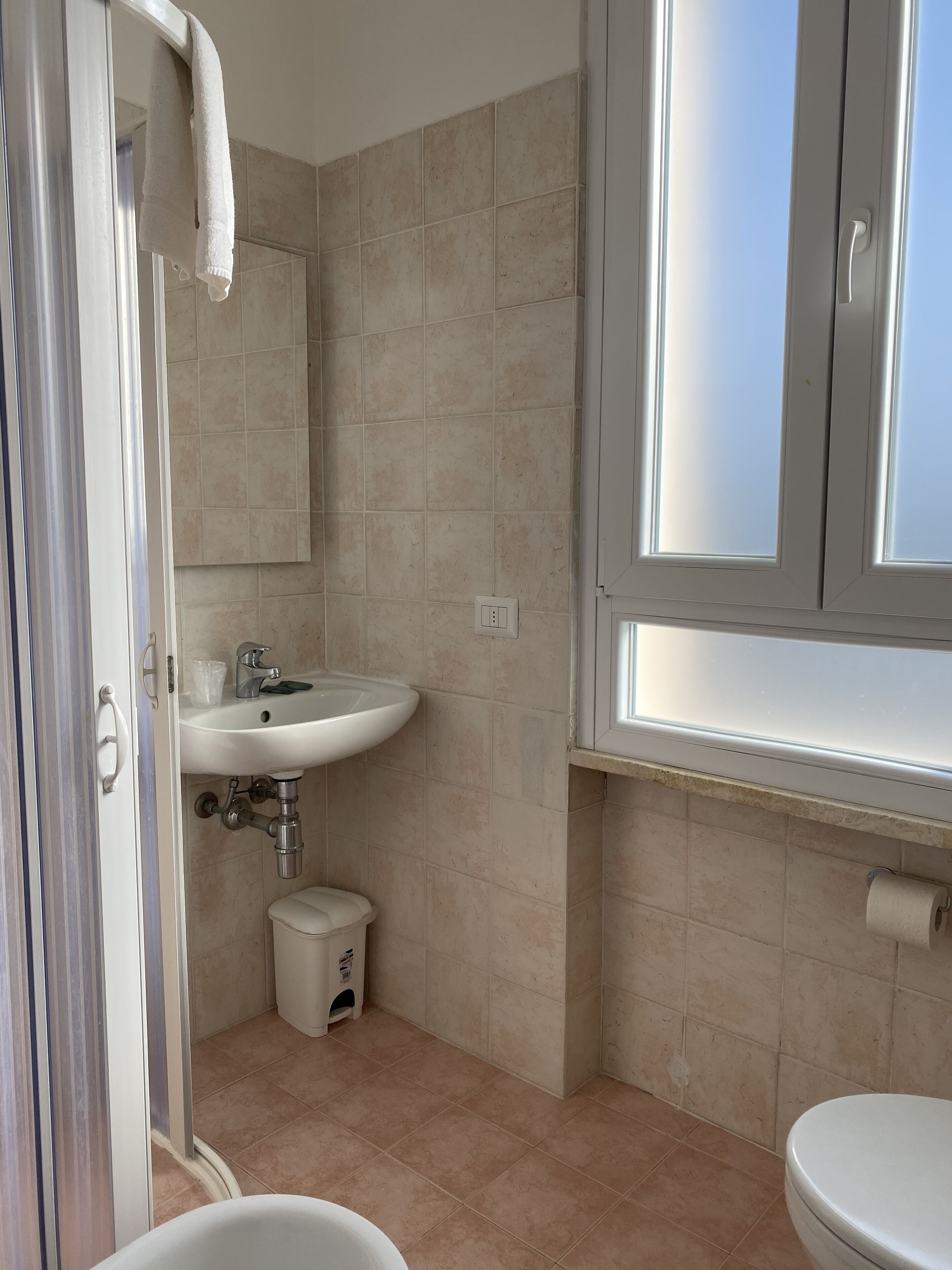 A bathroom with a sink, mirror, toilet, and a window.