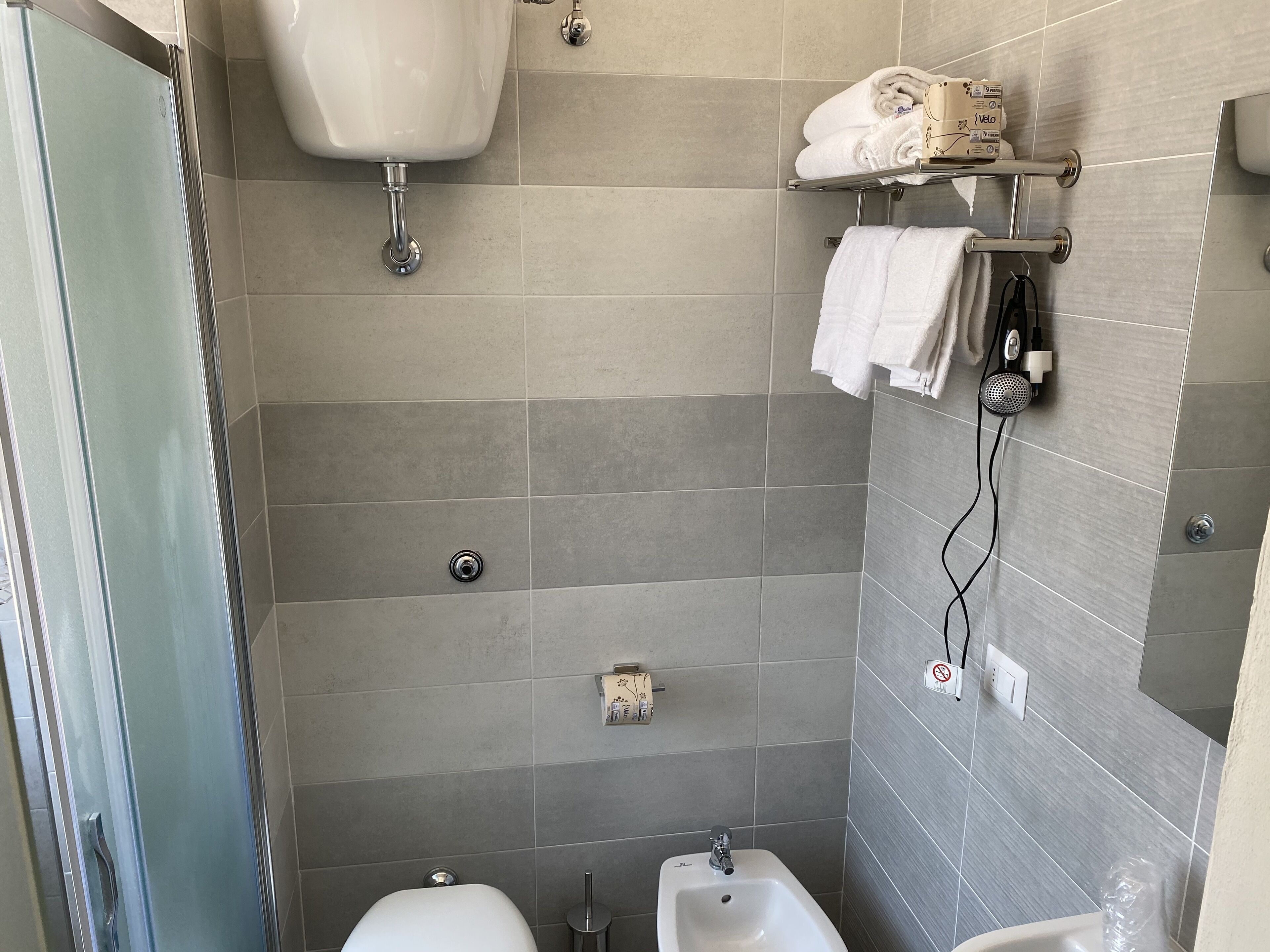 Egy modern fürőszoba üveg válaszfallal ellátott zuhanyzóval, fehér, lábazatos mosdókagylóval és WC-vel.