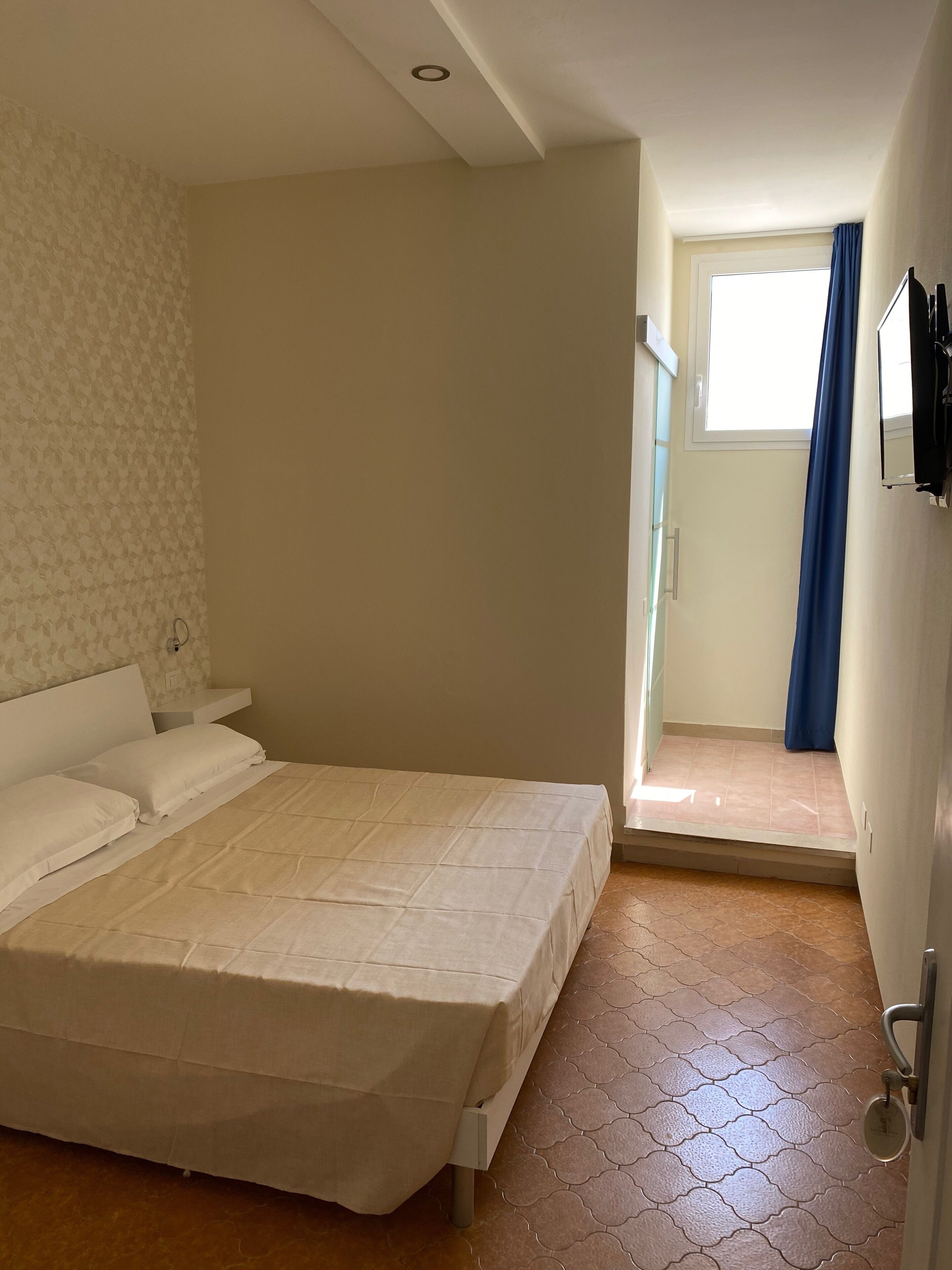 Un dormitorio con cama, ventana y puerta que da a un balcón.