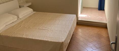 Un dormitorio con cama, ventana y puerta que da a un balcón.