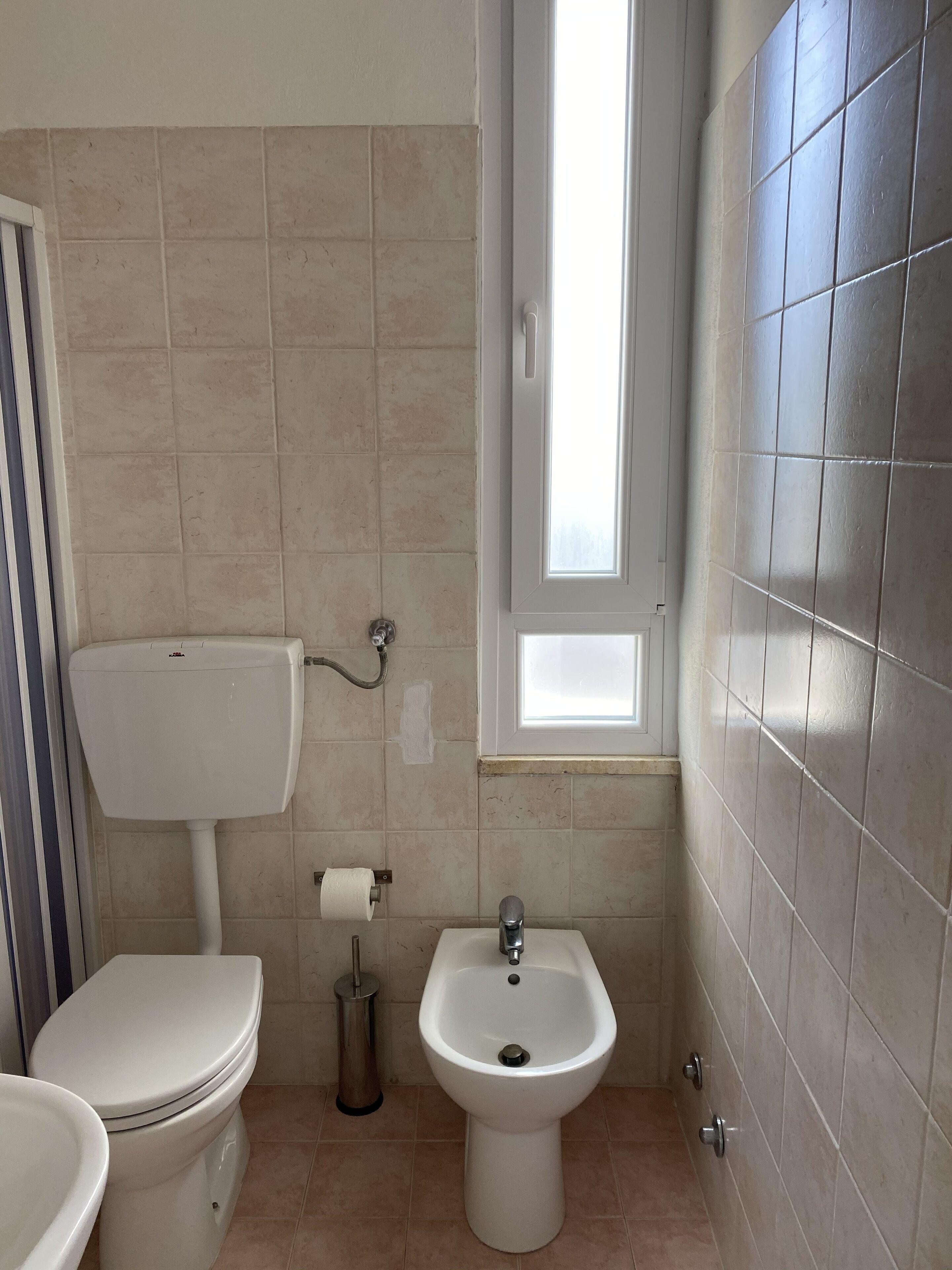 A small bathroom with a toilet, bidet, and a window.