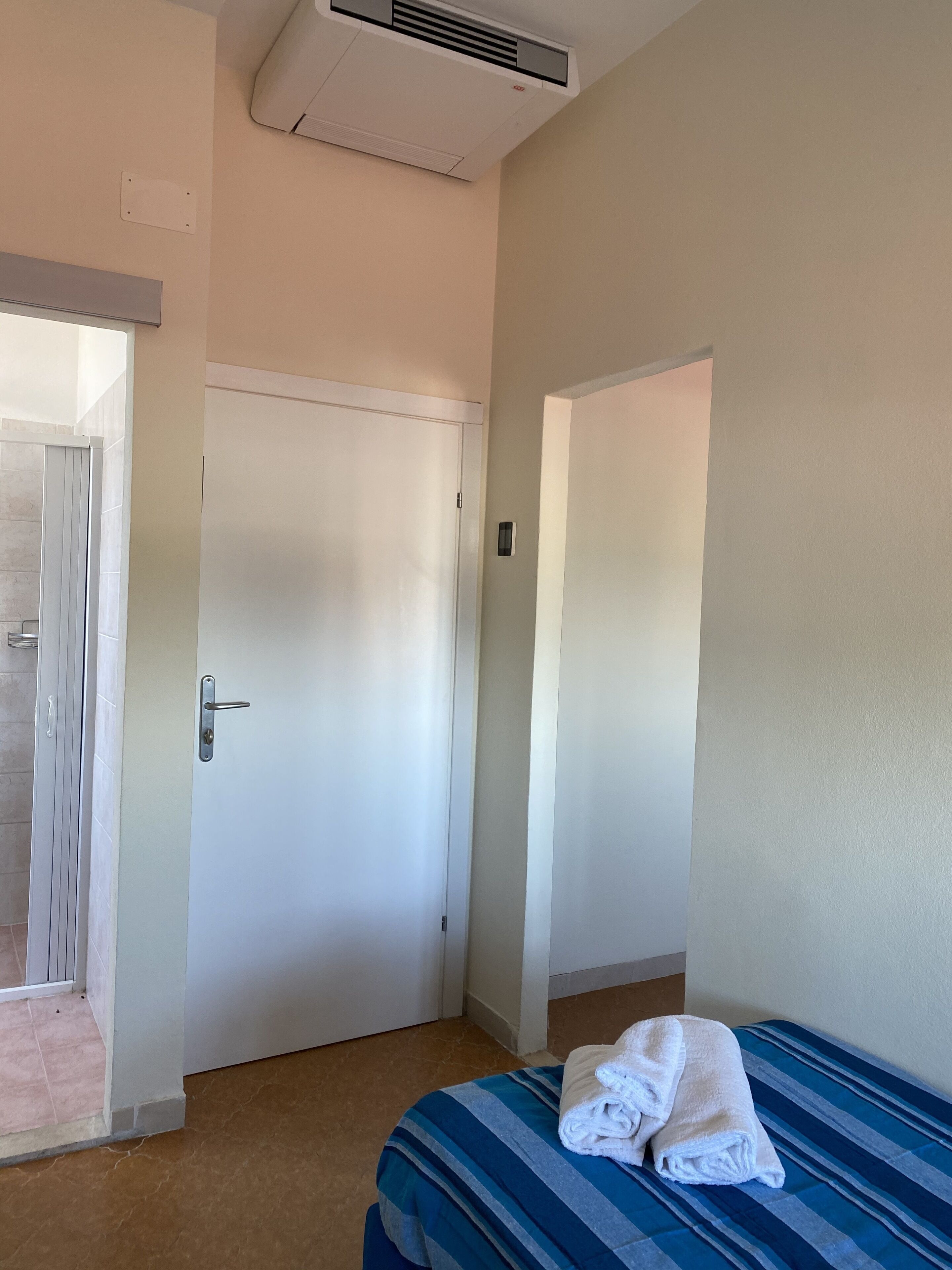 Una habitación de hotel con una cama, una puerta y un equipo de aire acondicionado.