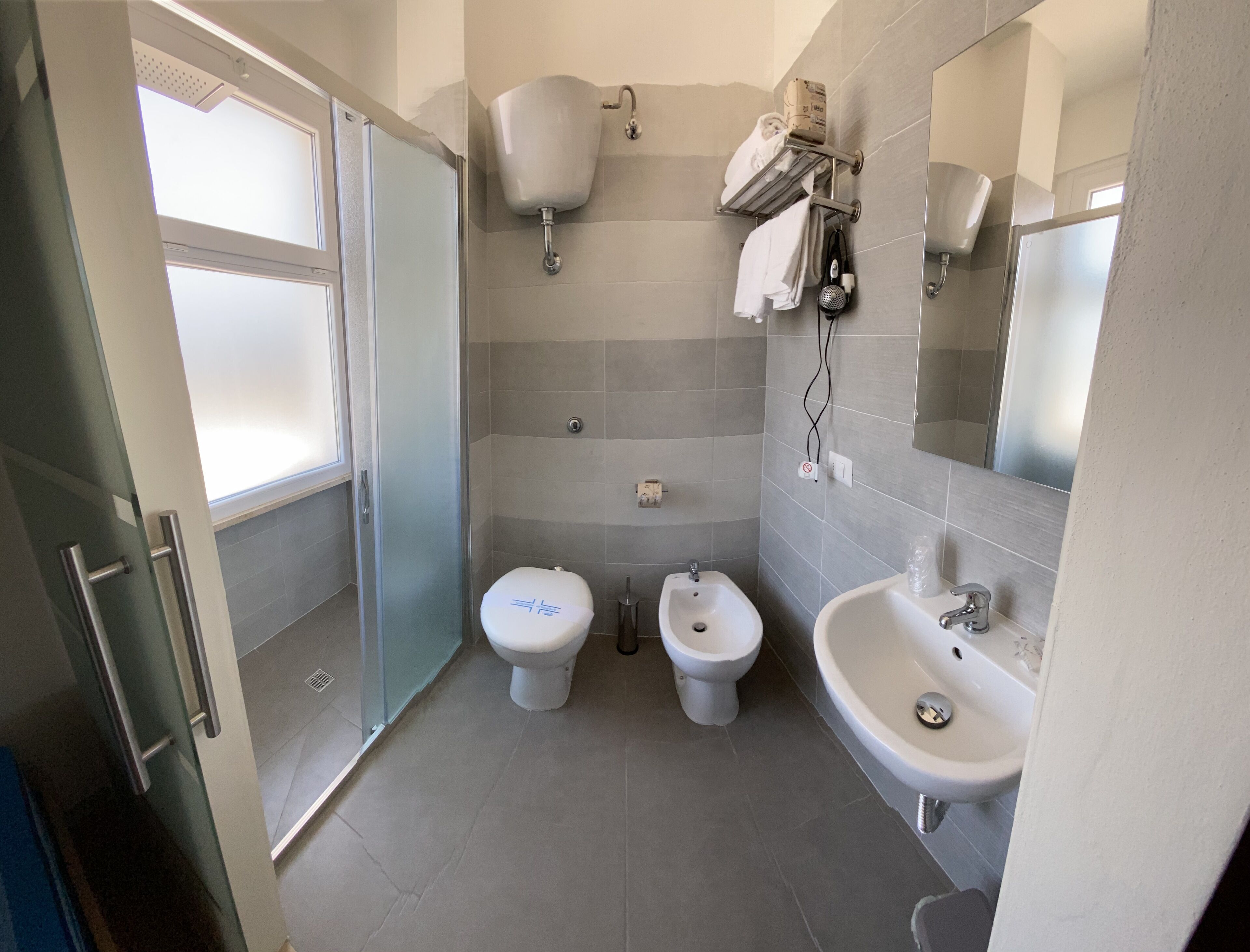Ein modernes Badezimmer mit Duschkabine aus Glas, zwei Toiletten, einem Bidet und einem Waschbecken.