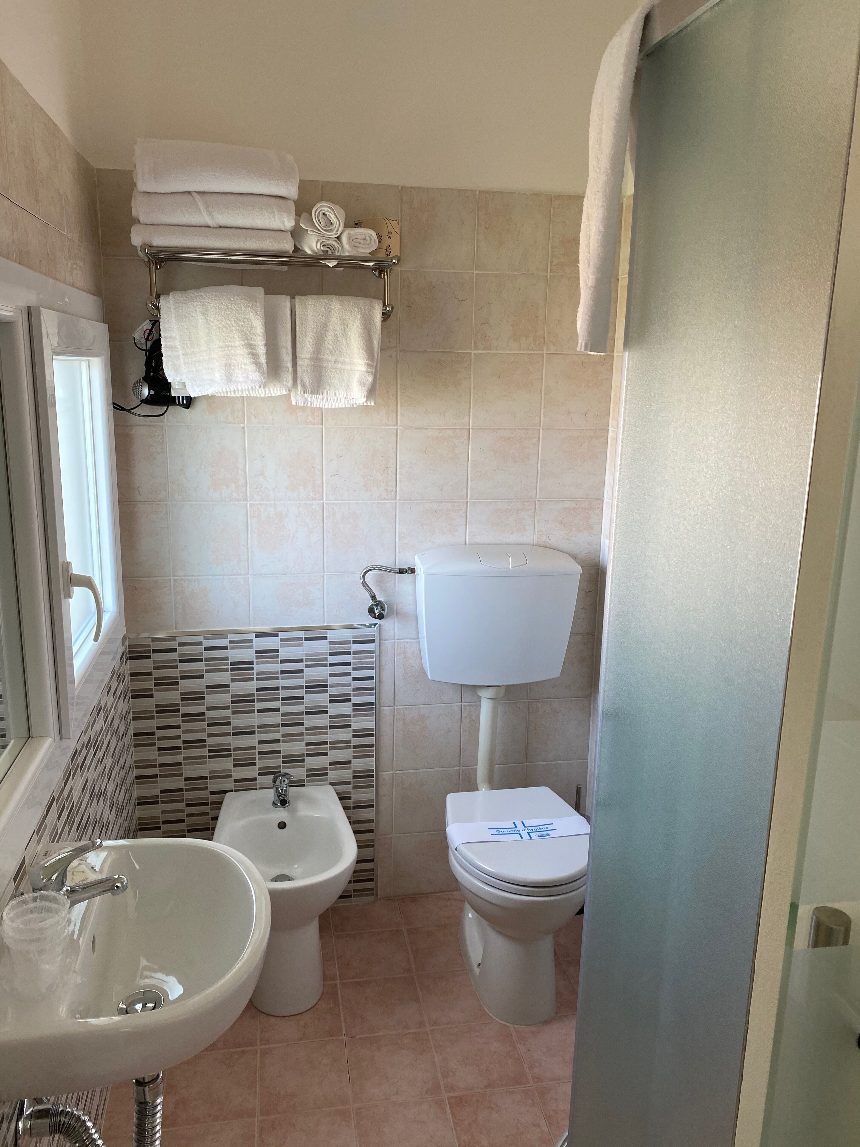 Een badkamer met een wastafel, bidet, toilet en een handdoekhouder met opgevouwen handdoeken.