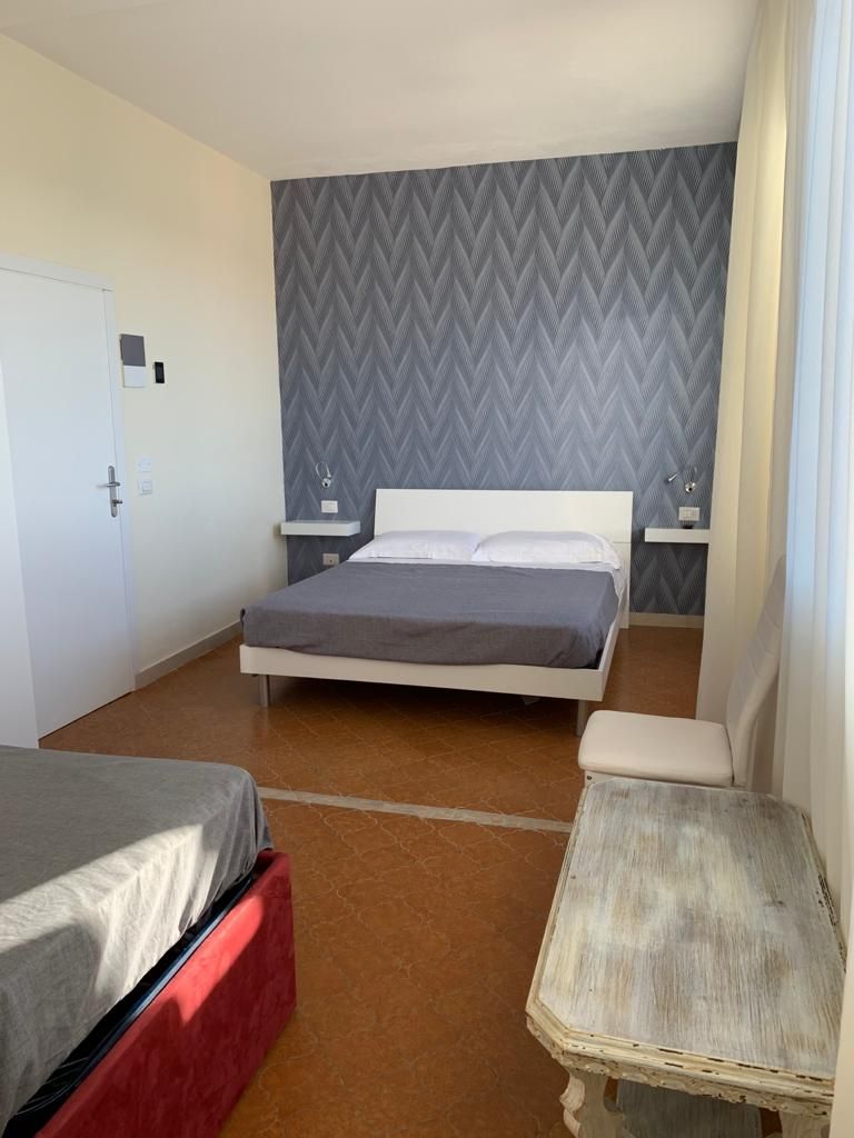 Un lit simple avec une tête de lit grise, une table de chevet et une petite table de nuit avec une lampe.