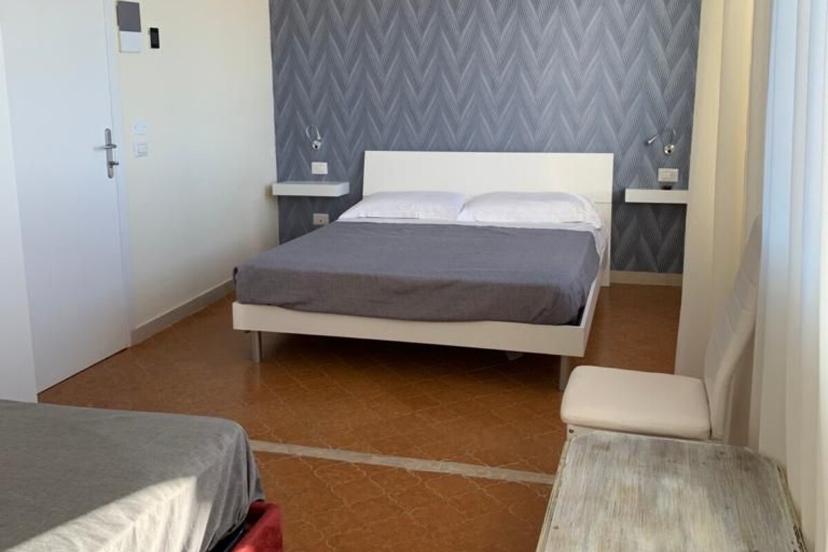Un dormitorio con cama, mesitas de noche, una pequeña mesa y una puerta.