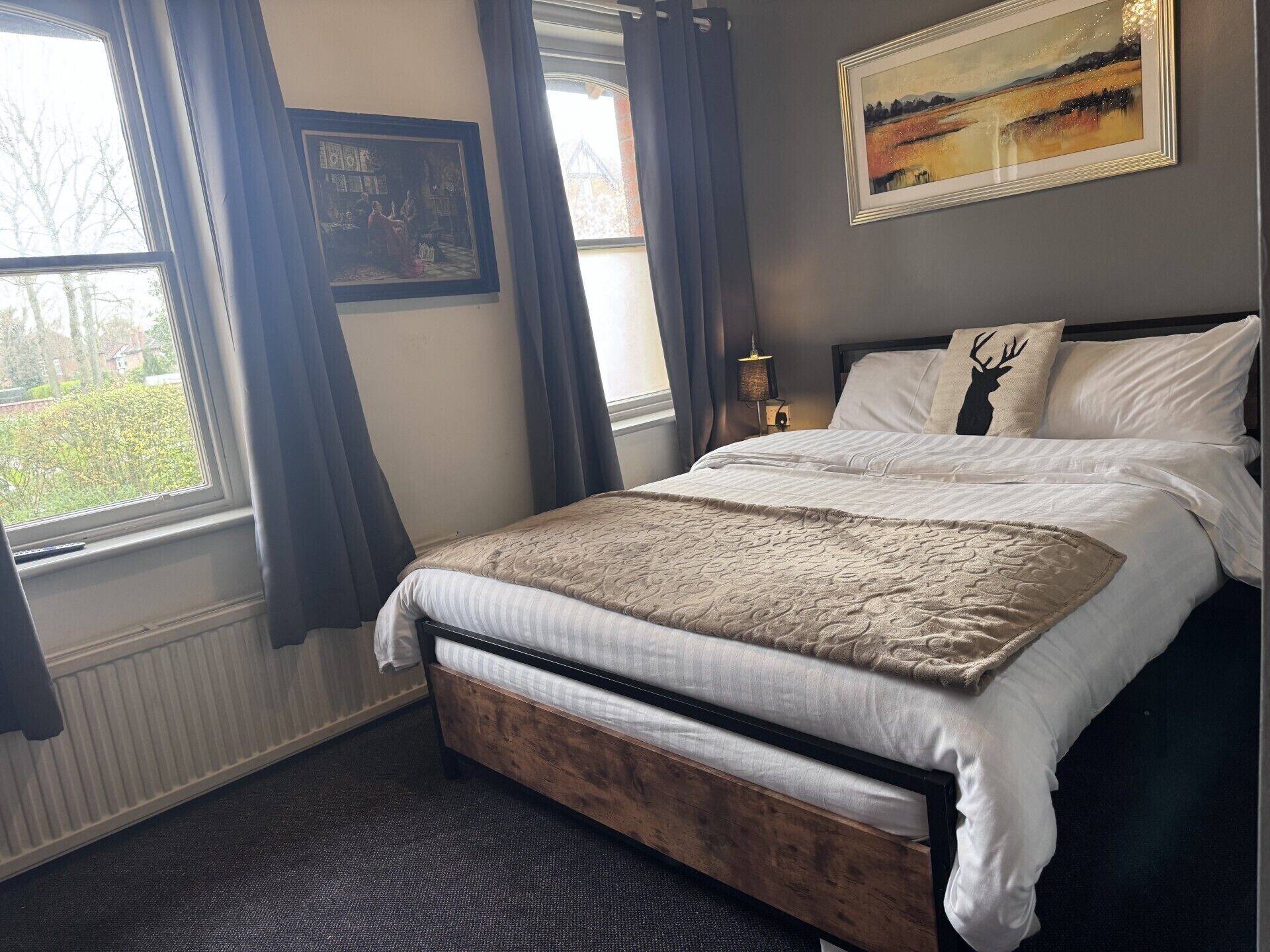 A bedroom with a bed, a window with curtains, a framed picture on the wall, and a lamp on the nightstand.