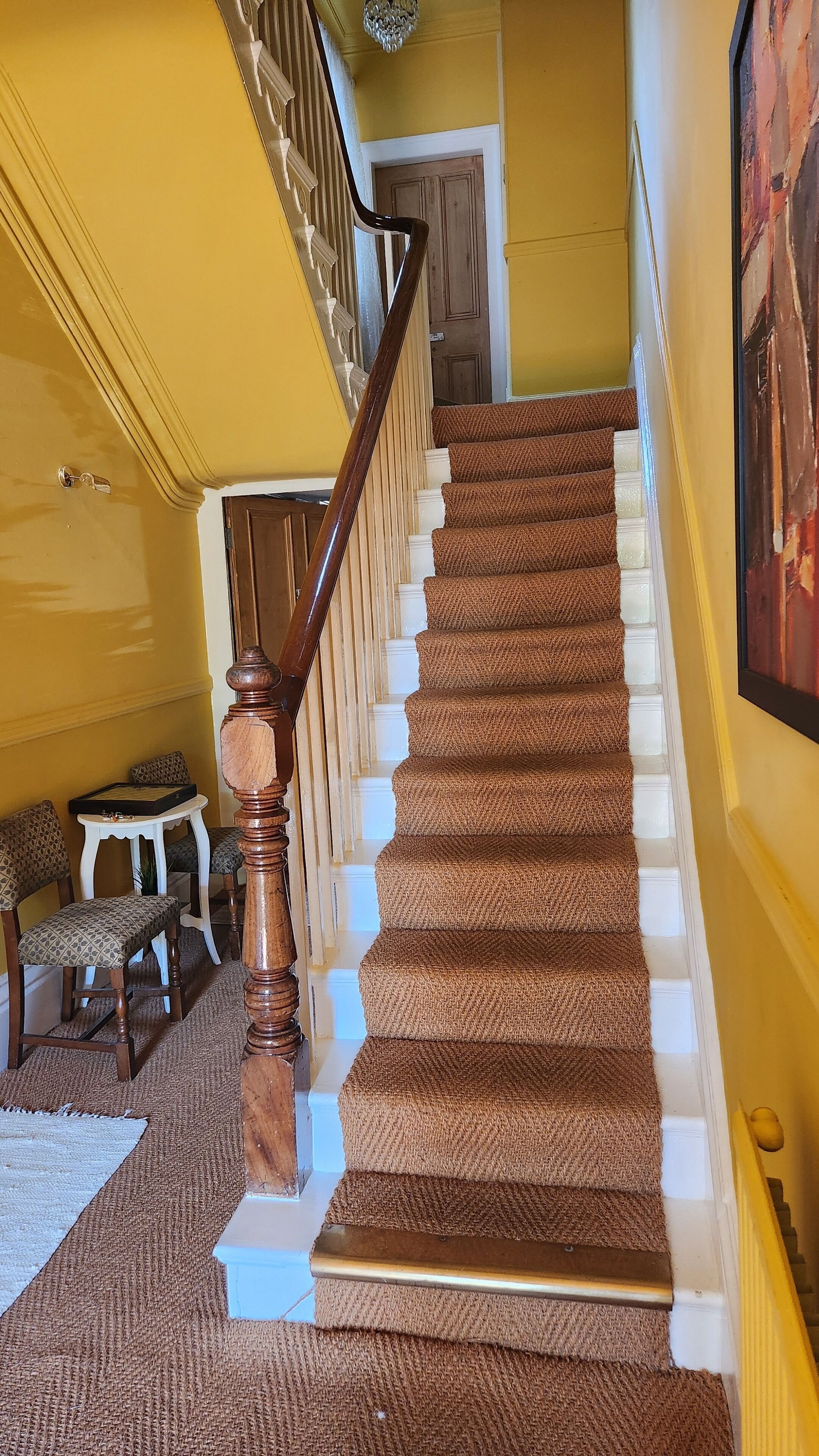 A staircase with a wooden handrail and carpeted steps leading to a door.