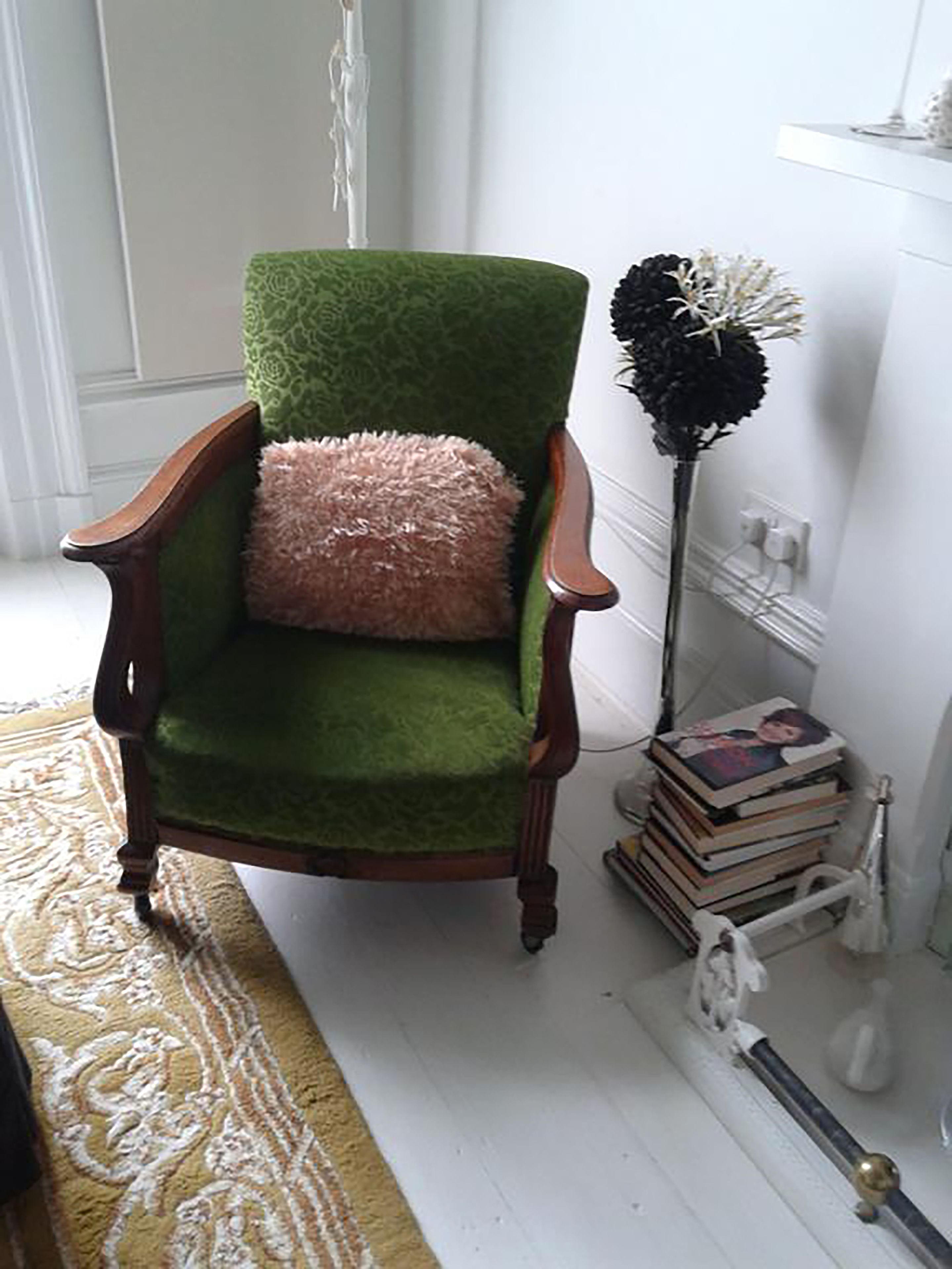 Un sillón verde con un cojín mullido, un adorno negro alto y una pila de libros sobre un soporte blanco.