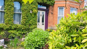 A brick building with ivy-covered walls and a well-maintained garden with various plants and a pathway. - OYO Cornerstone Manor Hotel (Sale)