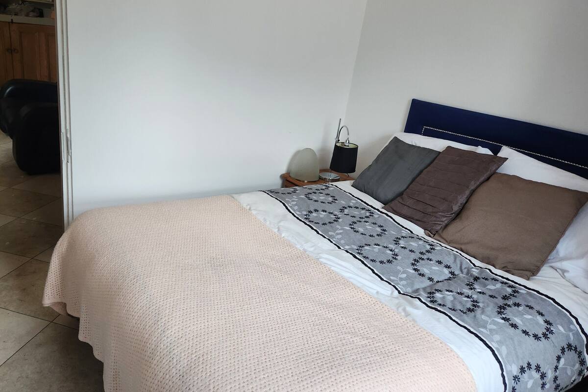 Ein ordentlich bezogenes Bett mit einem gemusterten Überwurf, ein Nachttisch mit Lampe und ein Holz-Kopfteil.