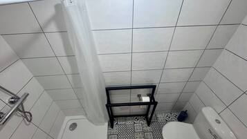 A small bathroom with a shower, toilet, and a sink with a hose.