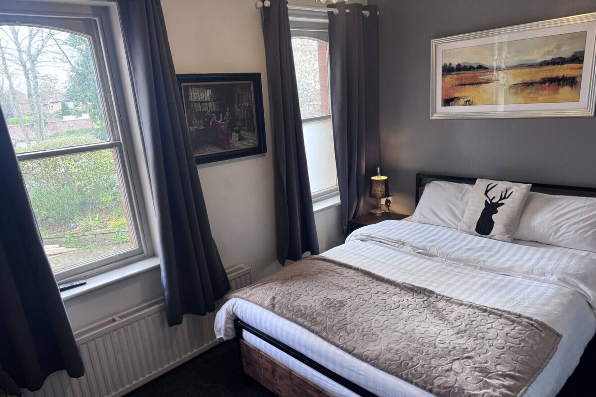 Ein Schlafzimmer mit Bett, Nachttischlampe, einem gerahmten Bild und einem Fenster mit Vorhängen.