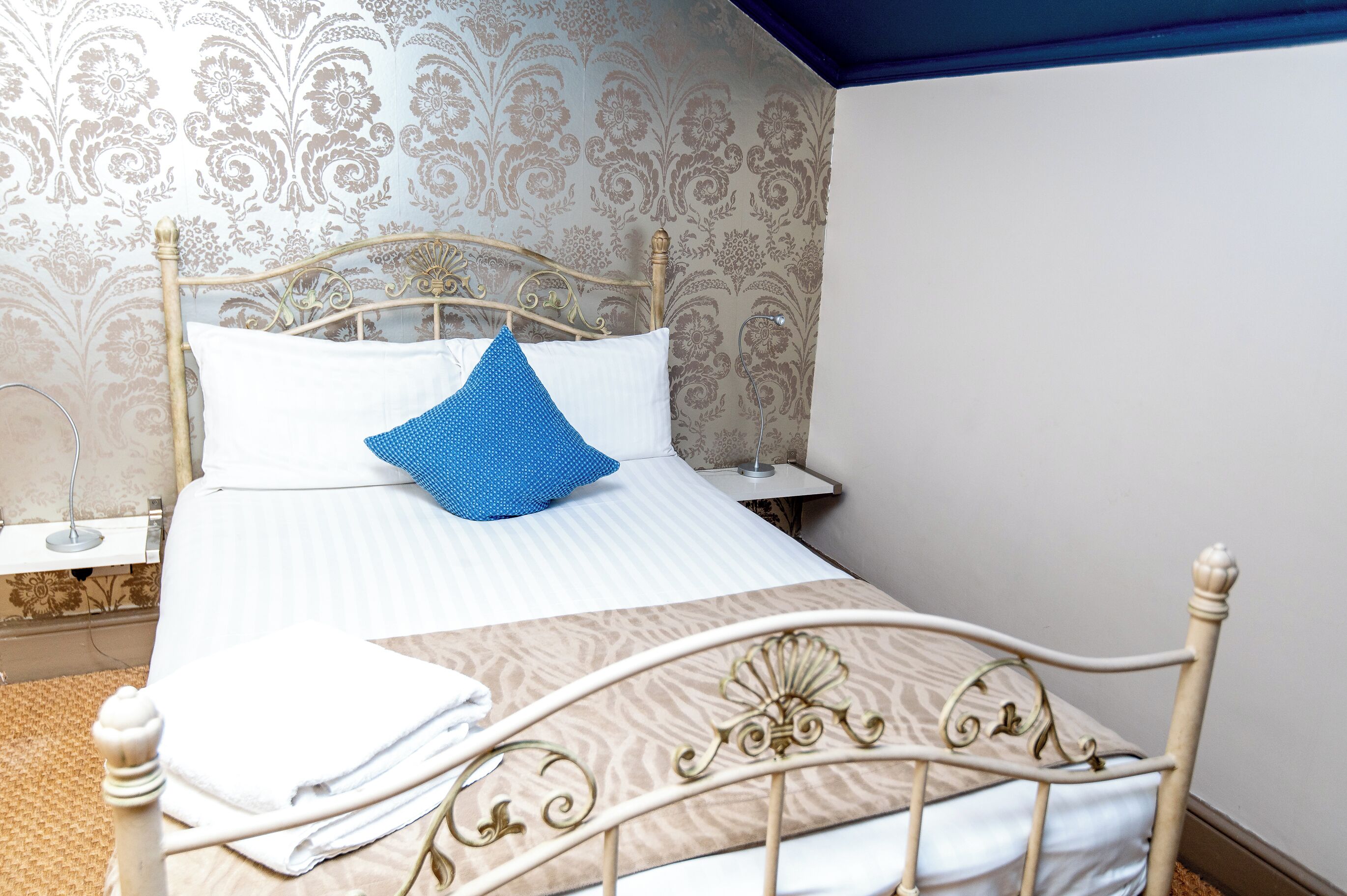 Una cama bien hecha con una almohada azul, una almohada blanca y una toalla blanca doblada.