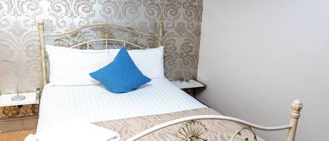 Una cama bien hecha con una almohada azul, una almohada blanca y una toalla blanca doblada.