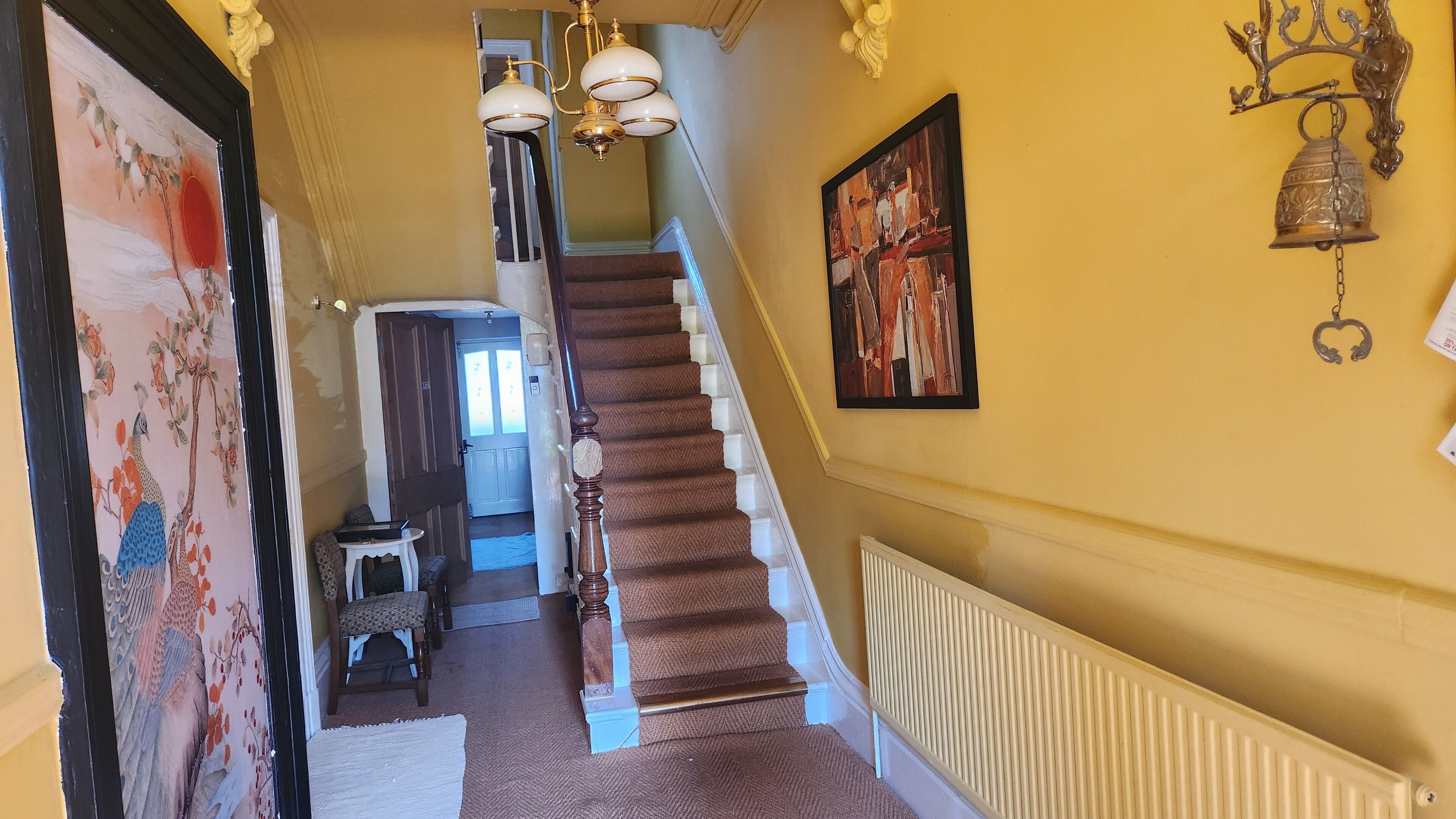 Una escalera con un rellano alfombrado, un radiador blanco y un timbre de pared.
