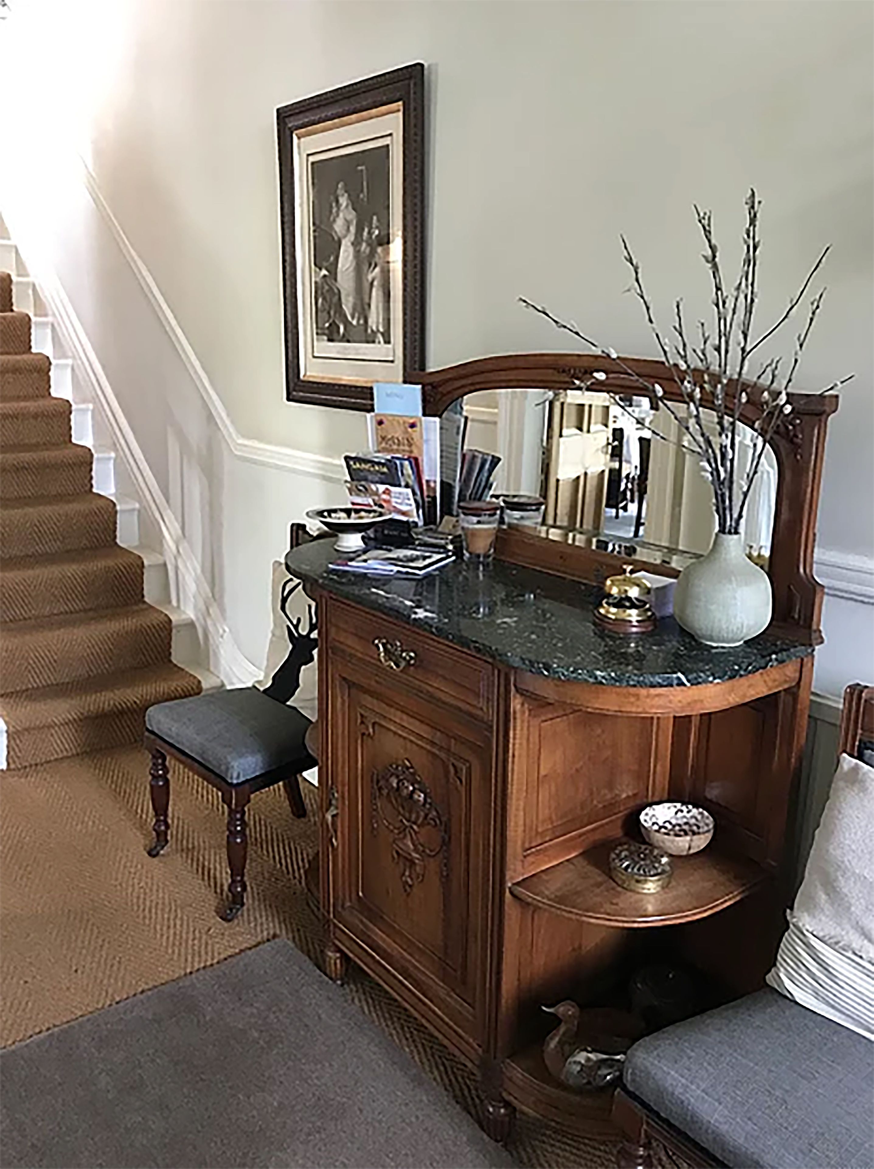 A wooden dresser with a mirror, a vase with branches, and a small shelf with decorative items.