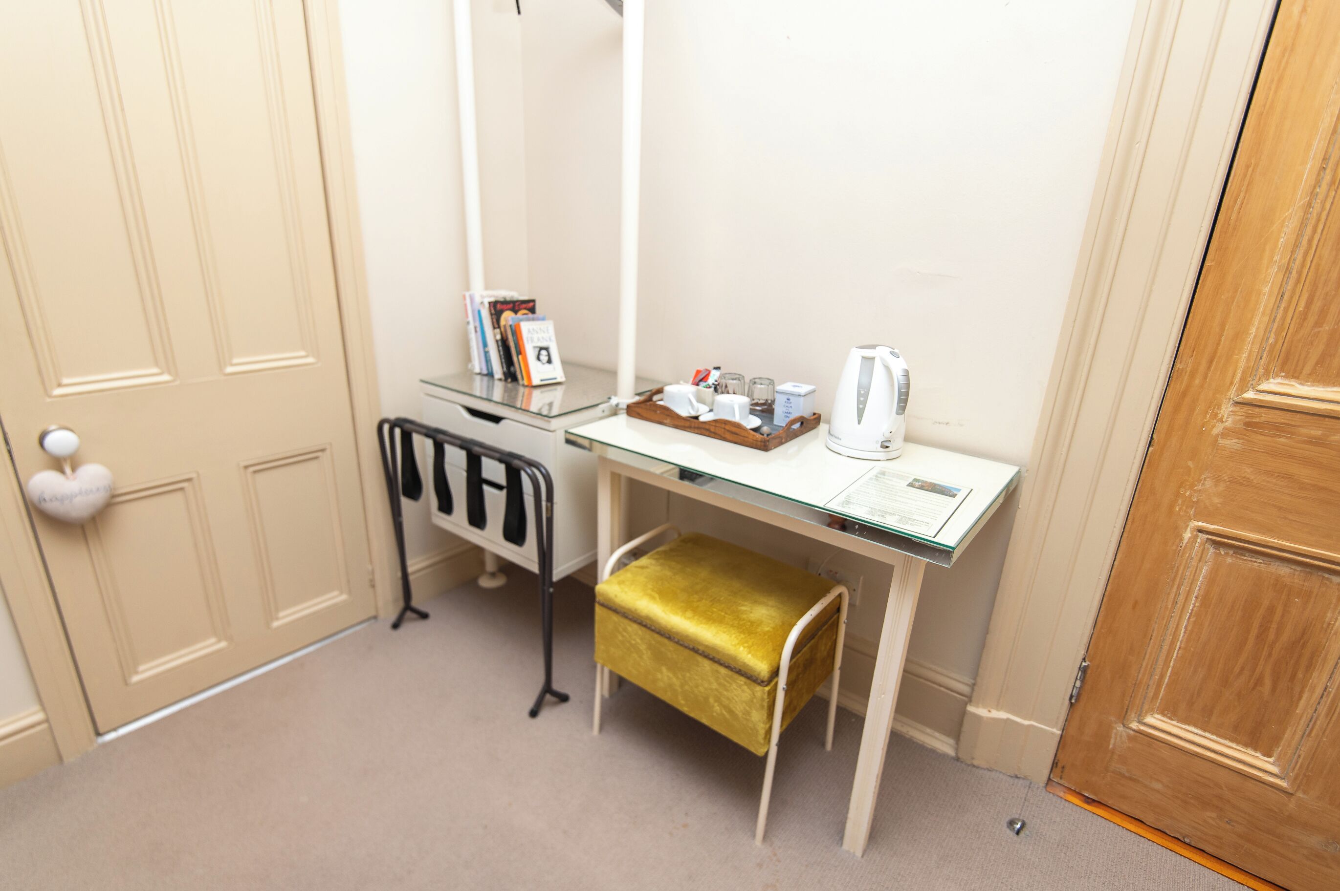 A small, compact room with a desk, a chair, a gold-colored ottoman, a mirror, and a wooden door.