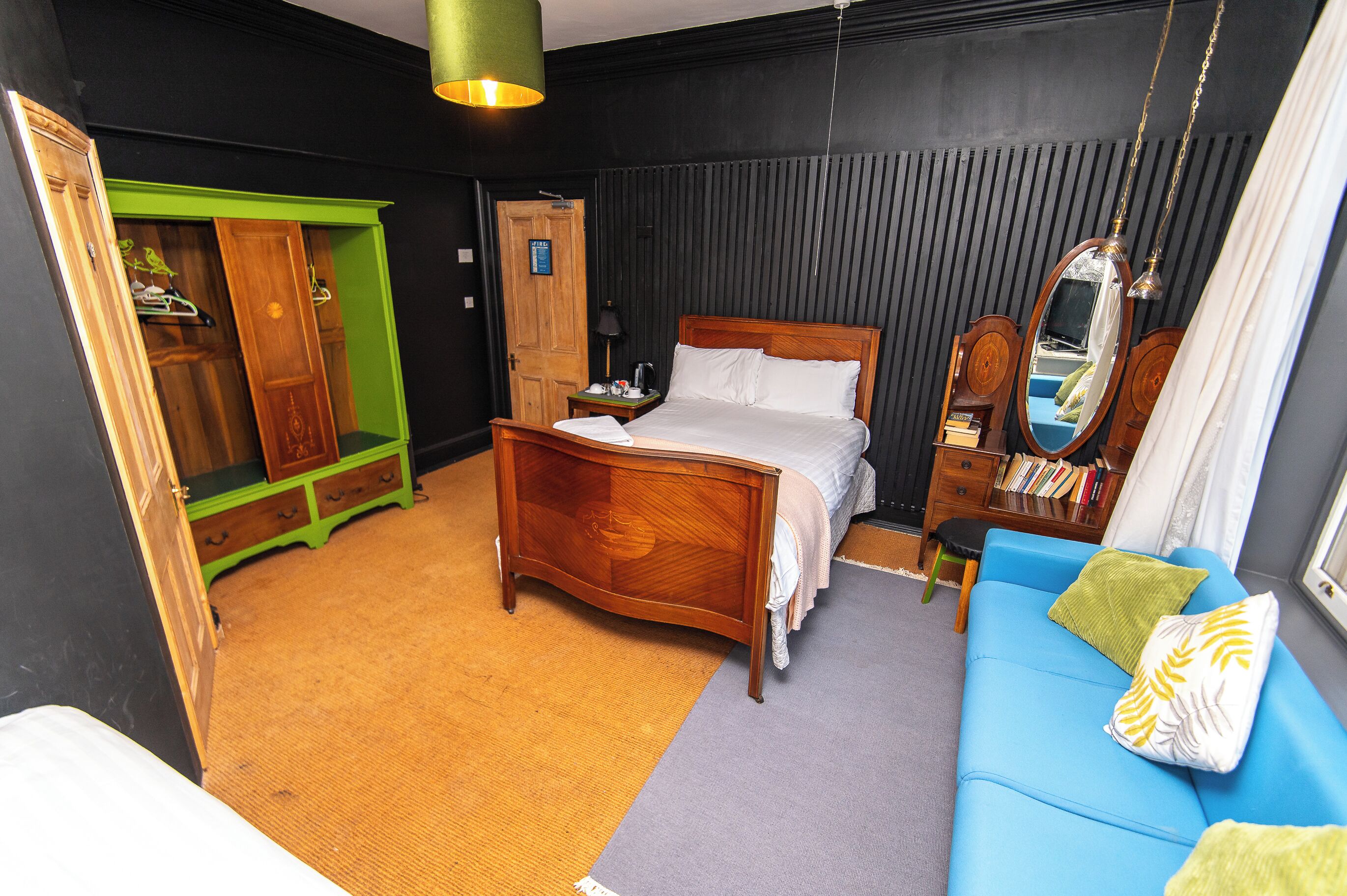 A bedroom with a bed, a blue sofa, a green wardrobe, and a mirror.