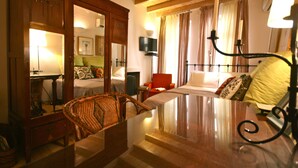 Una habitación de hotel con cama, una silla, un escritorio, televisor y ventana con cortinas.