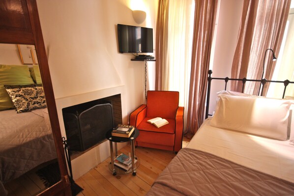 A hotel room with a bed, a chair, a television, and a small table with books. - Delightful two-bedroom house with sun terrace in the heart of Chania Old Town. (Χανιά)