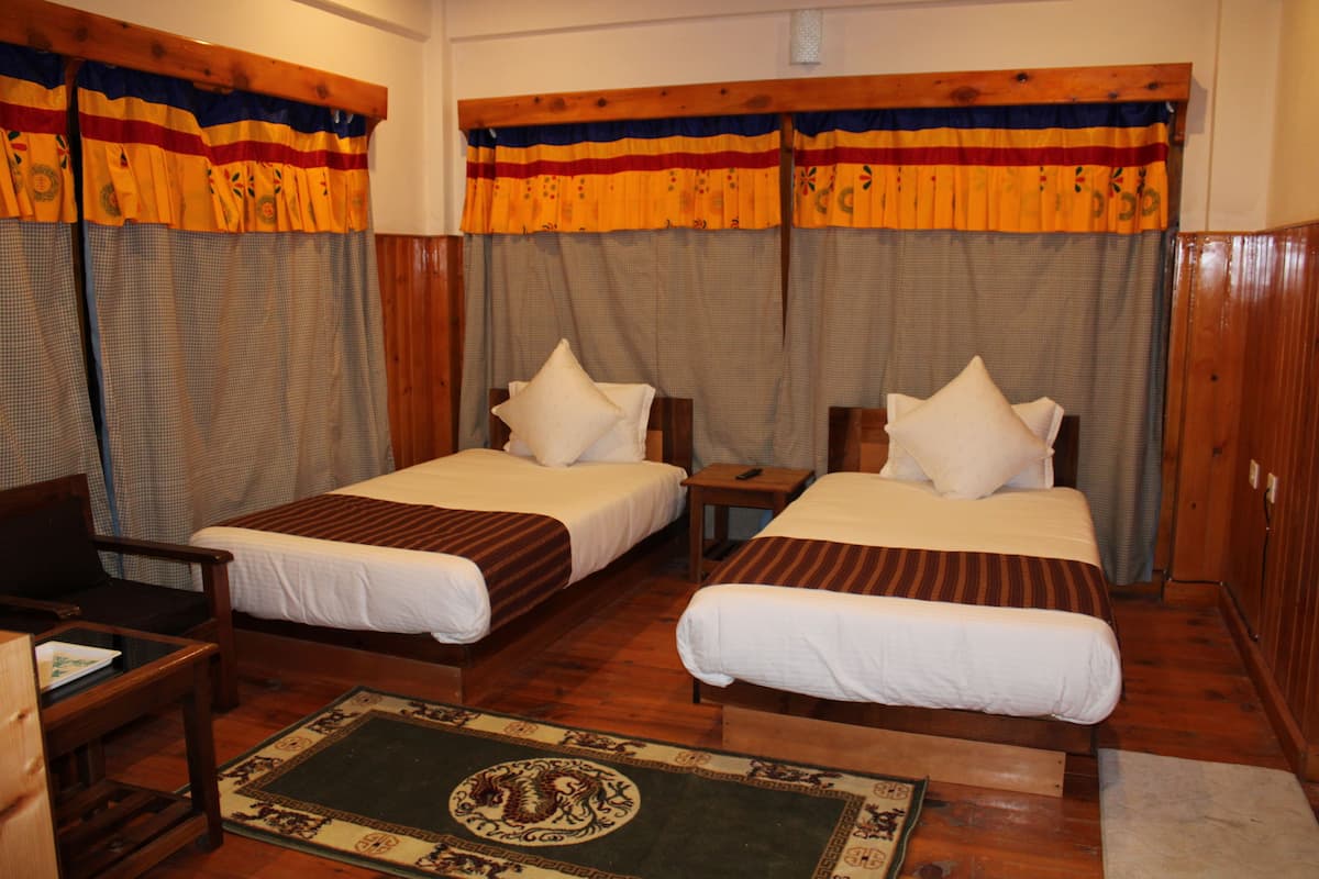 A room with two single beds, wooden headboards, a small table, and a chair.