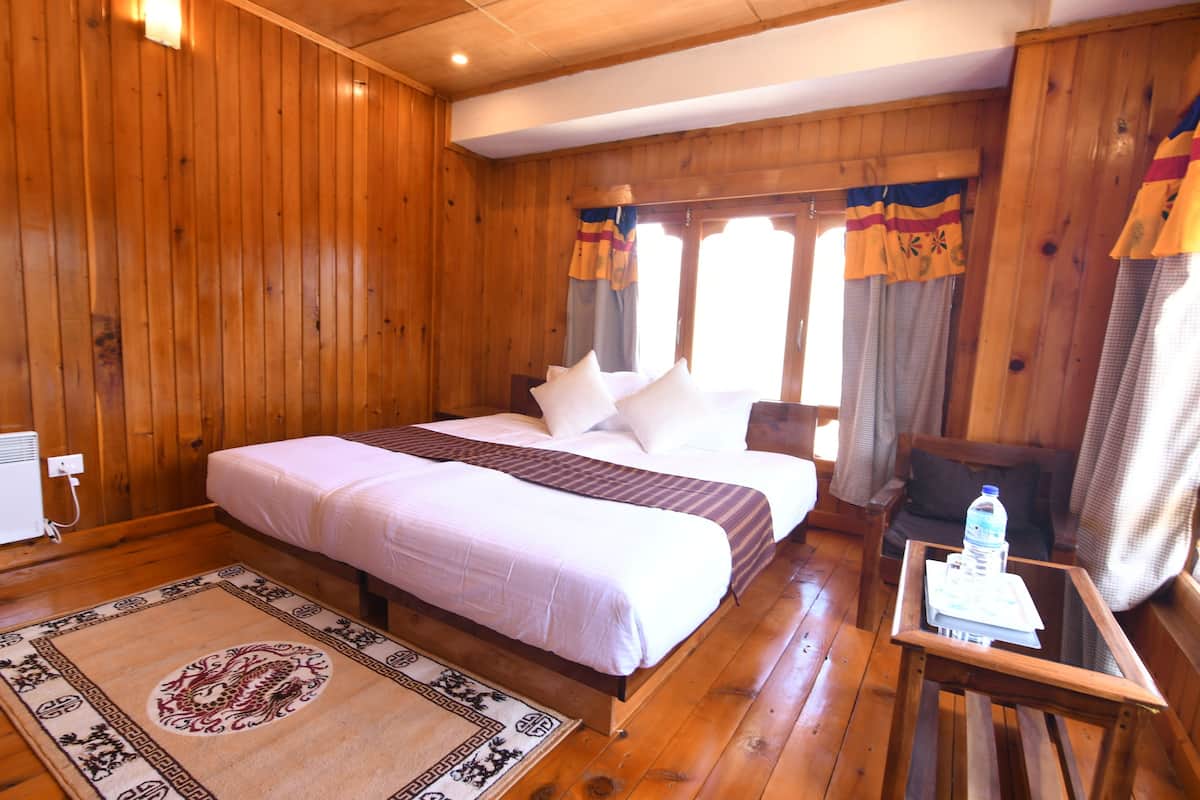 A wooden-paneled room with a bed, a small table with a water bottle, and a chair.