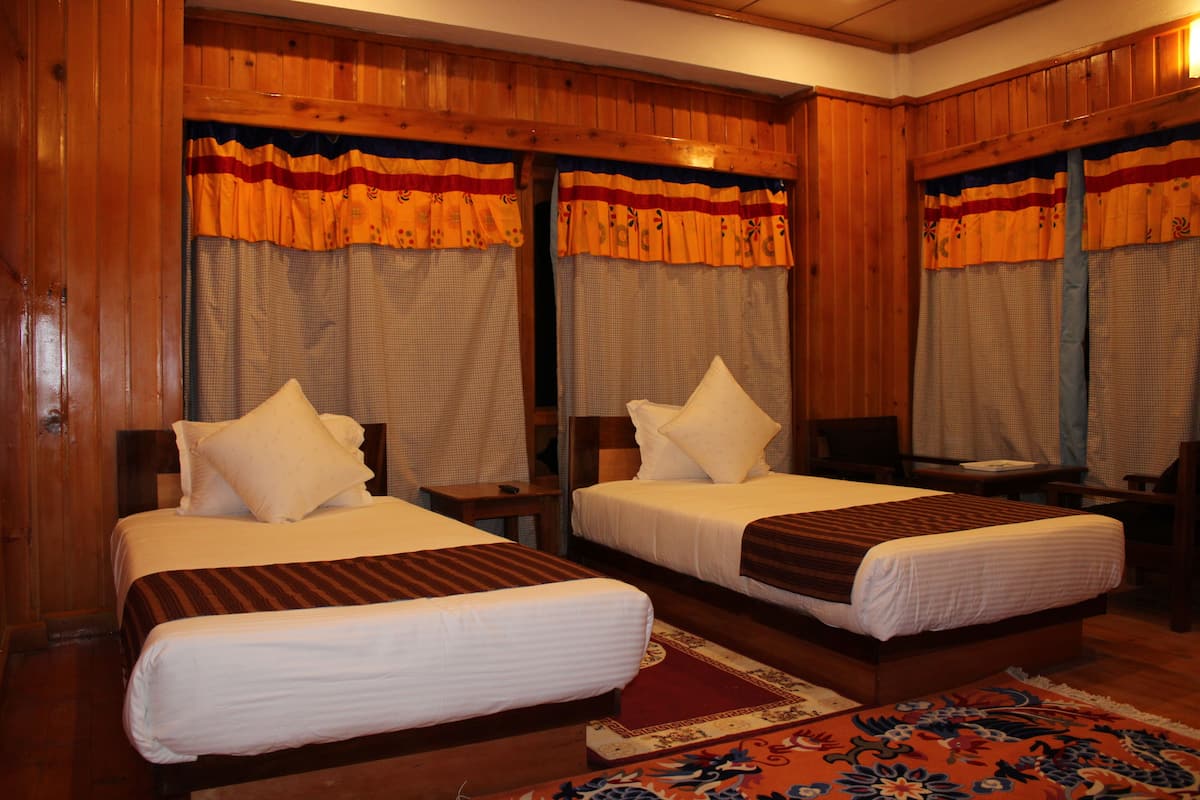 A hotel room with two single beds, wooden paneling, and a patterned rug.