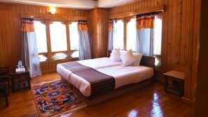 Una habitación de madera con una cama grande, una mesita y un ventanal con cortinas.