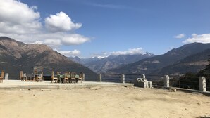 Un comedor con mesas y sillas, vistas a montañas y cielo despejado.