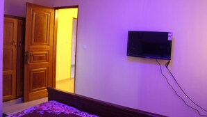 A bedroom with a bed, a television mounted on the wall, and a wooden door. - Ndancy Hotel (Ebolowa)