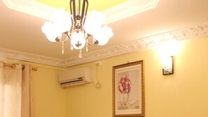 A living room with a brown leather sofa, a glass coffee table with flowers, a flat-screen TV on a wooden stand, a framed picture on the wall, and a ceiling light fixture. - Ndancy Hotel (Ebolowa)