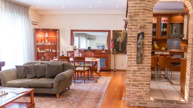 Una sala de estar con sofá, una mesa de centro y un comedor con sillas y una mesa. Se ve una cocina a través de un arco.