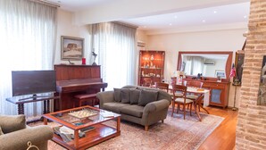 Una sala de estar con sofá, mesa de centro, televisor, piano y un área de comedor con sillas y alfombra.