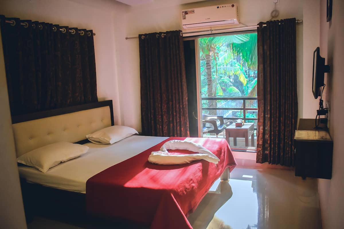 A hotel room with a bed, a red bedspread, a white pillow, a window with curtains, and an air conditioning unit.
