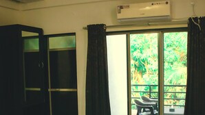 A hotel room with a bed, a ceiling fan, an air conditioning unit, a sliding glass door leading to an outdoor area with a table and chairs. - Royal Paradise Hotel (Alibag)