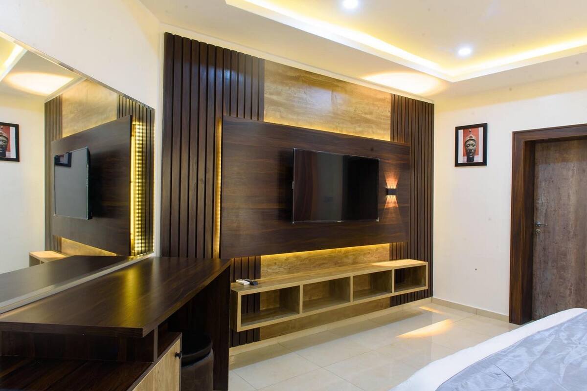 A modern bedroom with a large bed, a built-in TV, and a wooden entertainment unit.