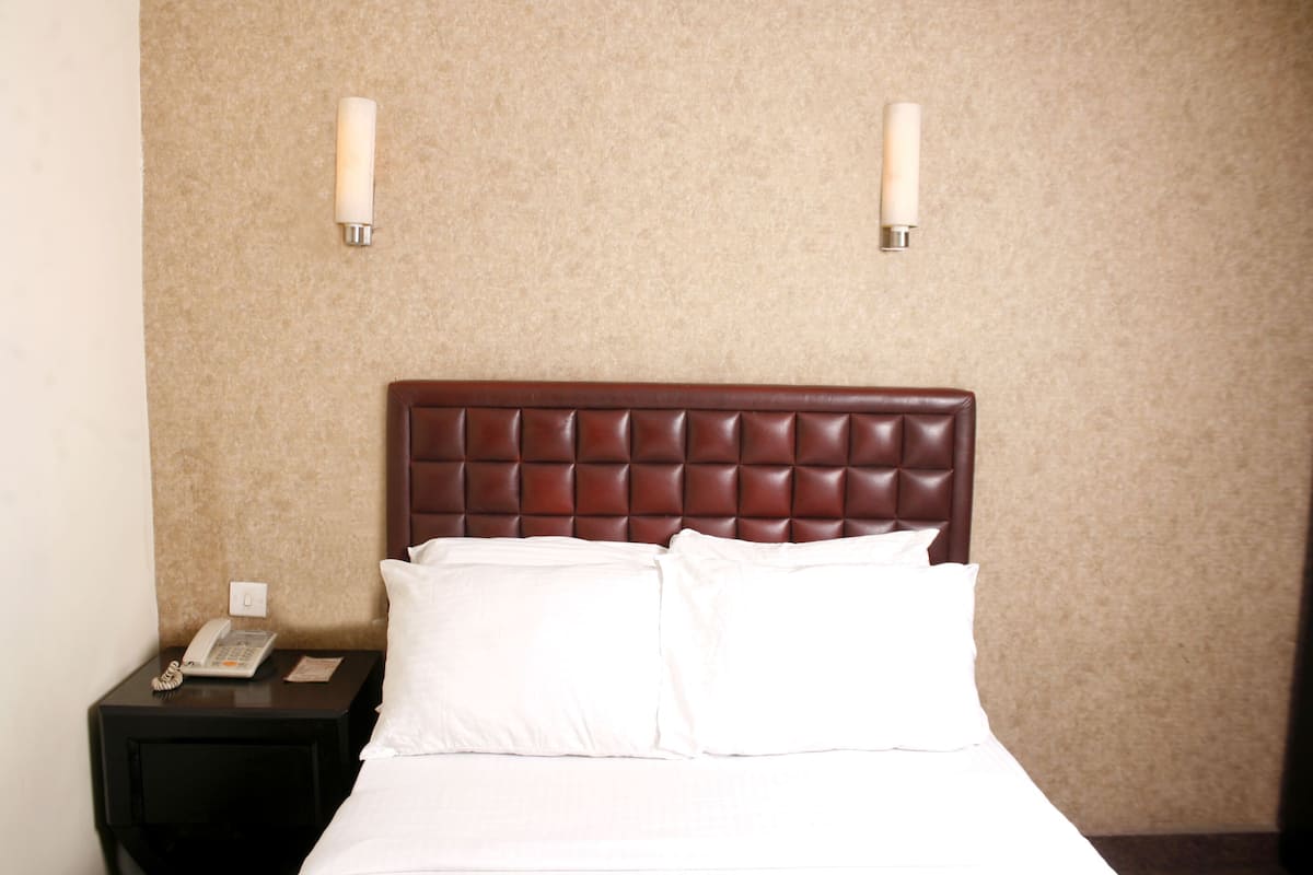 A hotel room with a bed, white linens, a brown headboard, a nightstand with a phone, and two wall-mounted light fixtures.