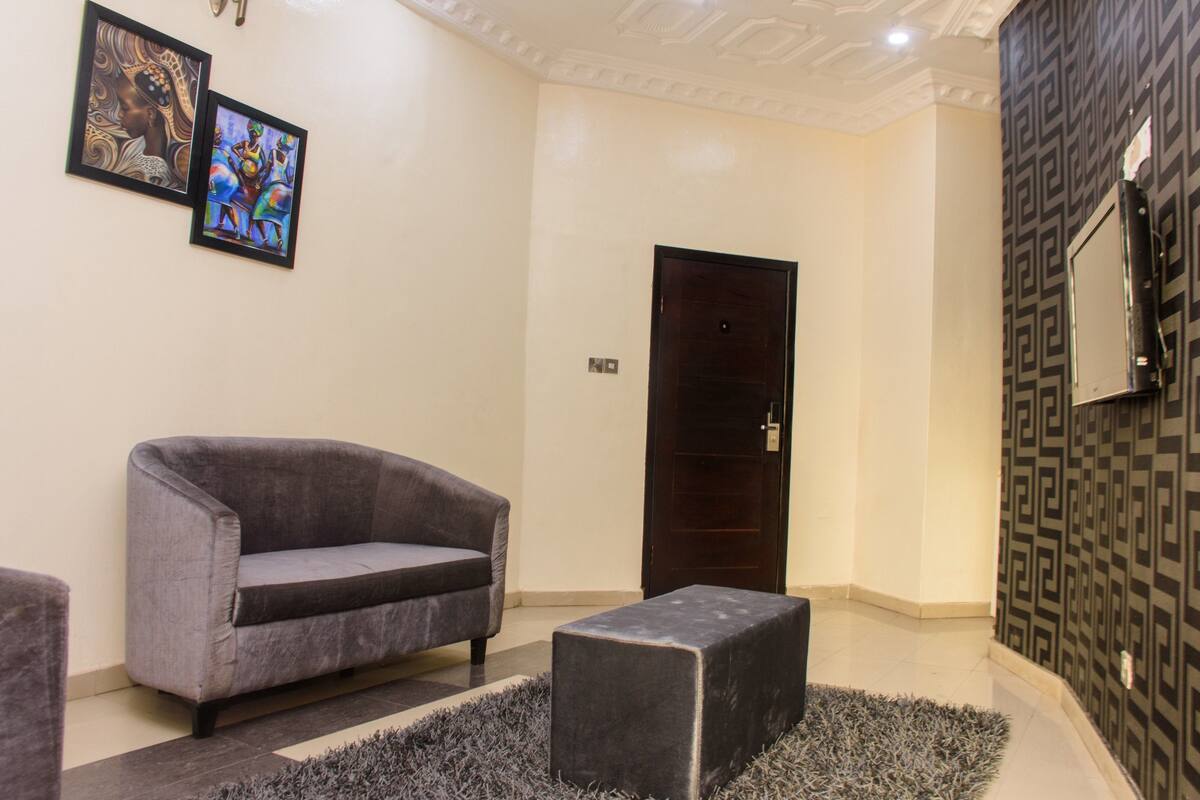 A modern lobby with a grey sofa, a dark wooden door, and a patterned wall.